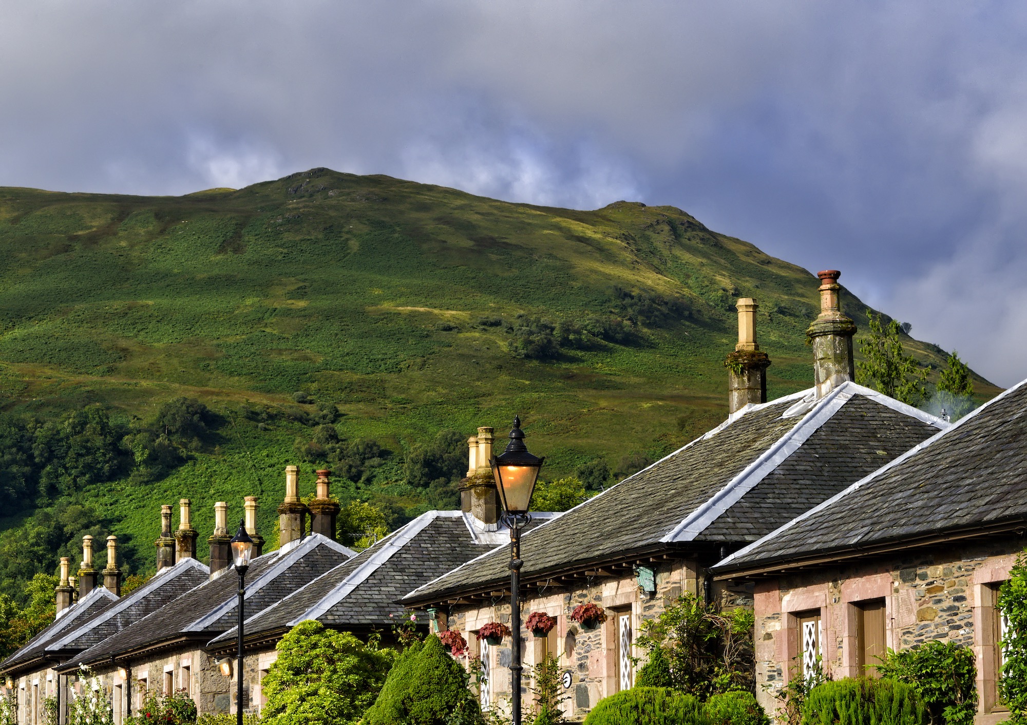 A row of houses. Behind them is a tall green hill