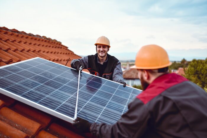 Men on an orange tiled rood installing solar panels.