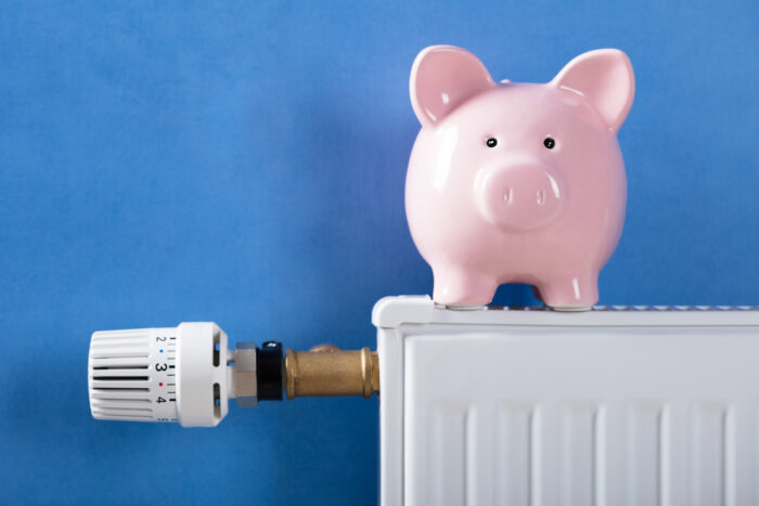 A piggy bank on a radiator. The radiator has a thermostatic radiator valve