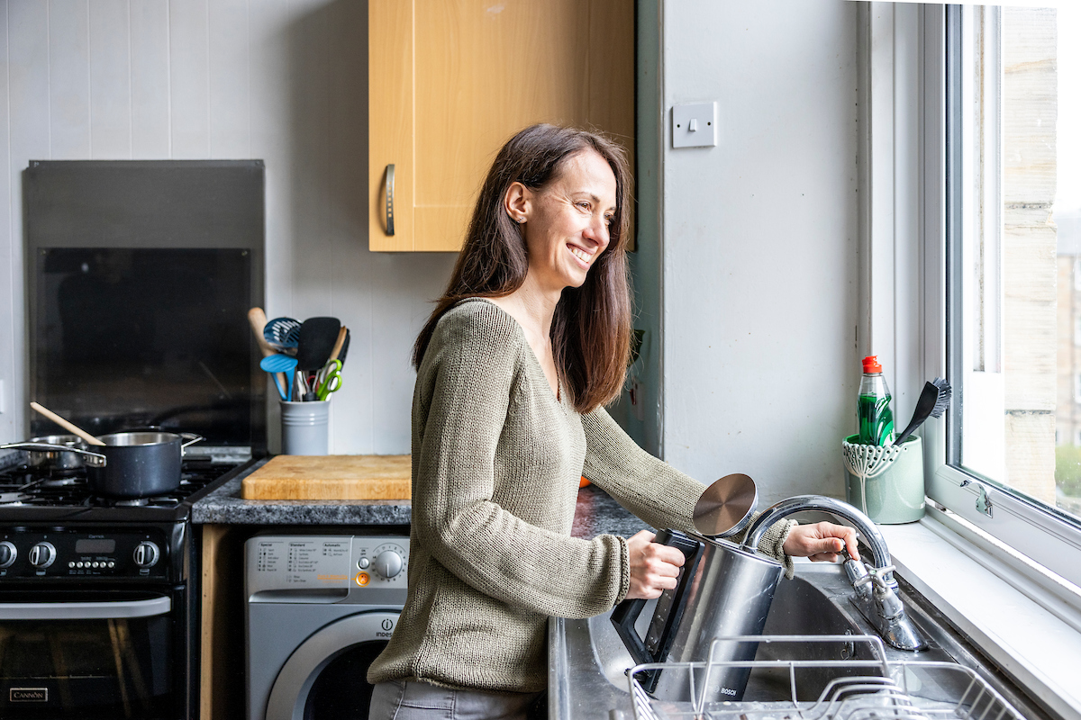 A woman stands by her sink in her kitchen.