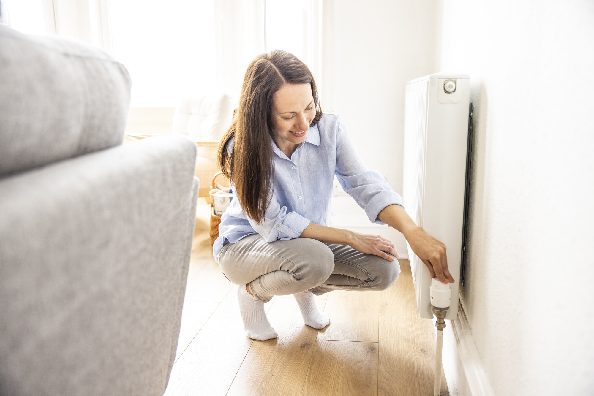 A woman adjusts the temperature valve on a radiator.