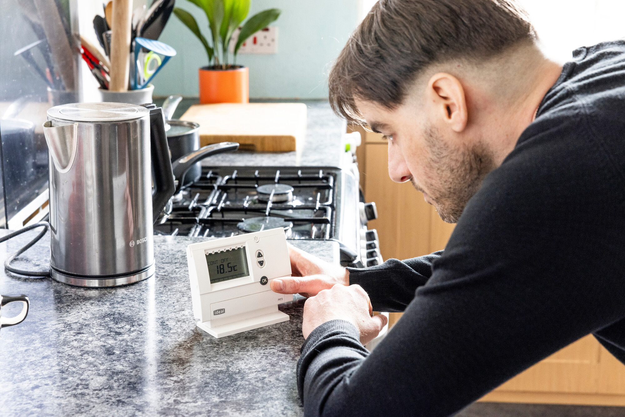 A man looks at his energy smart meter in the kitchen with his kettle in the background.