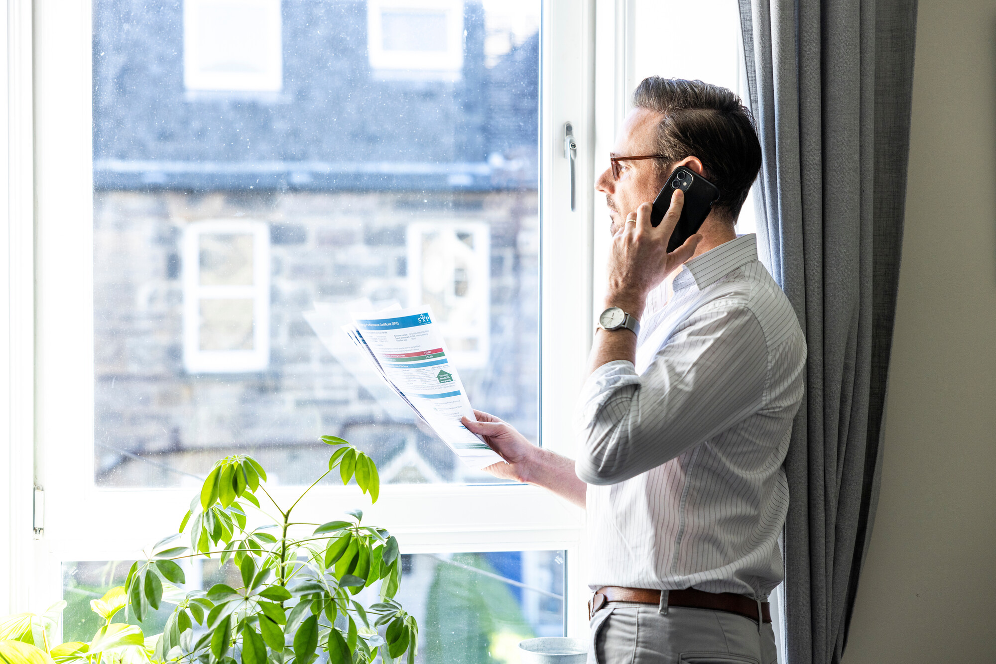 A man looks out of the window whilst talking on the phone.