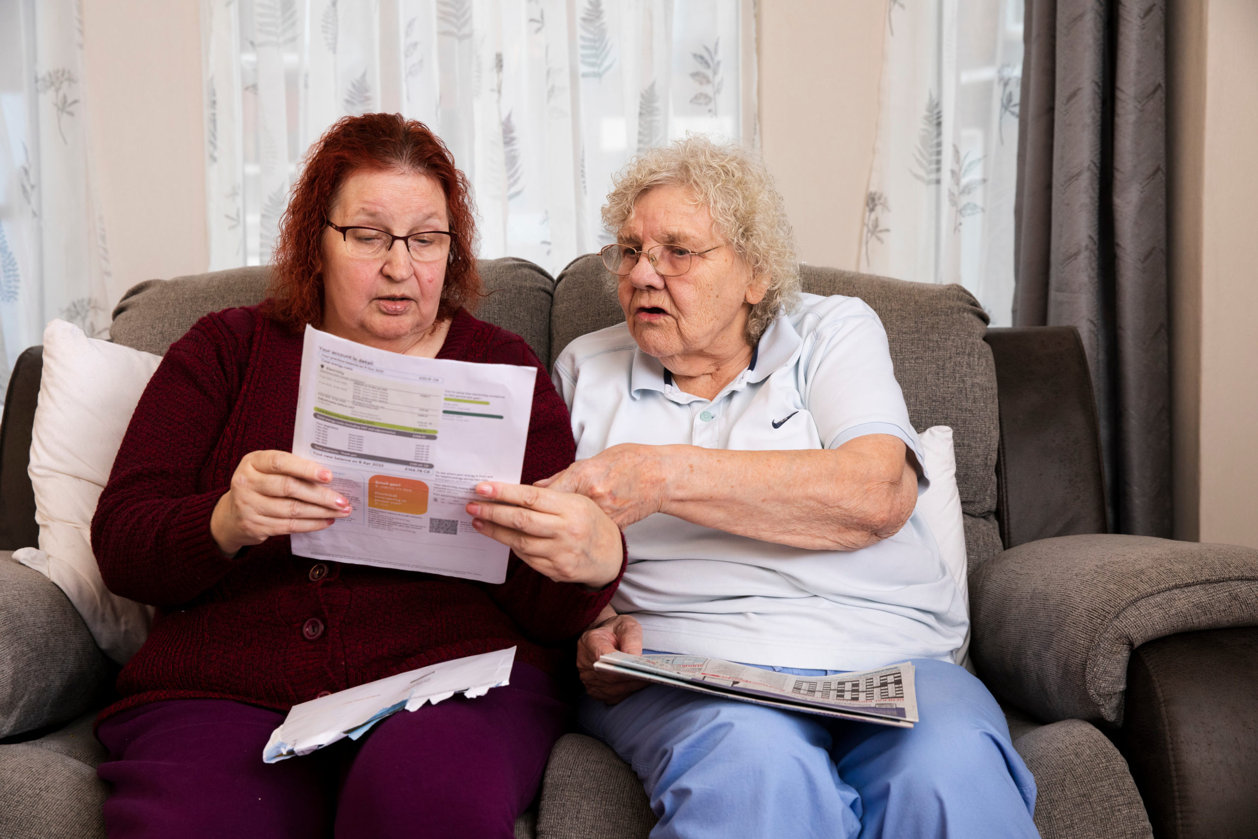 Two women sitting on a sofa, looking at an energy bill