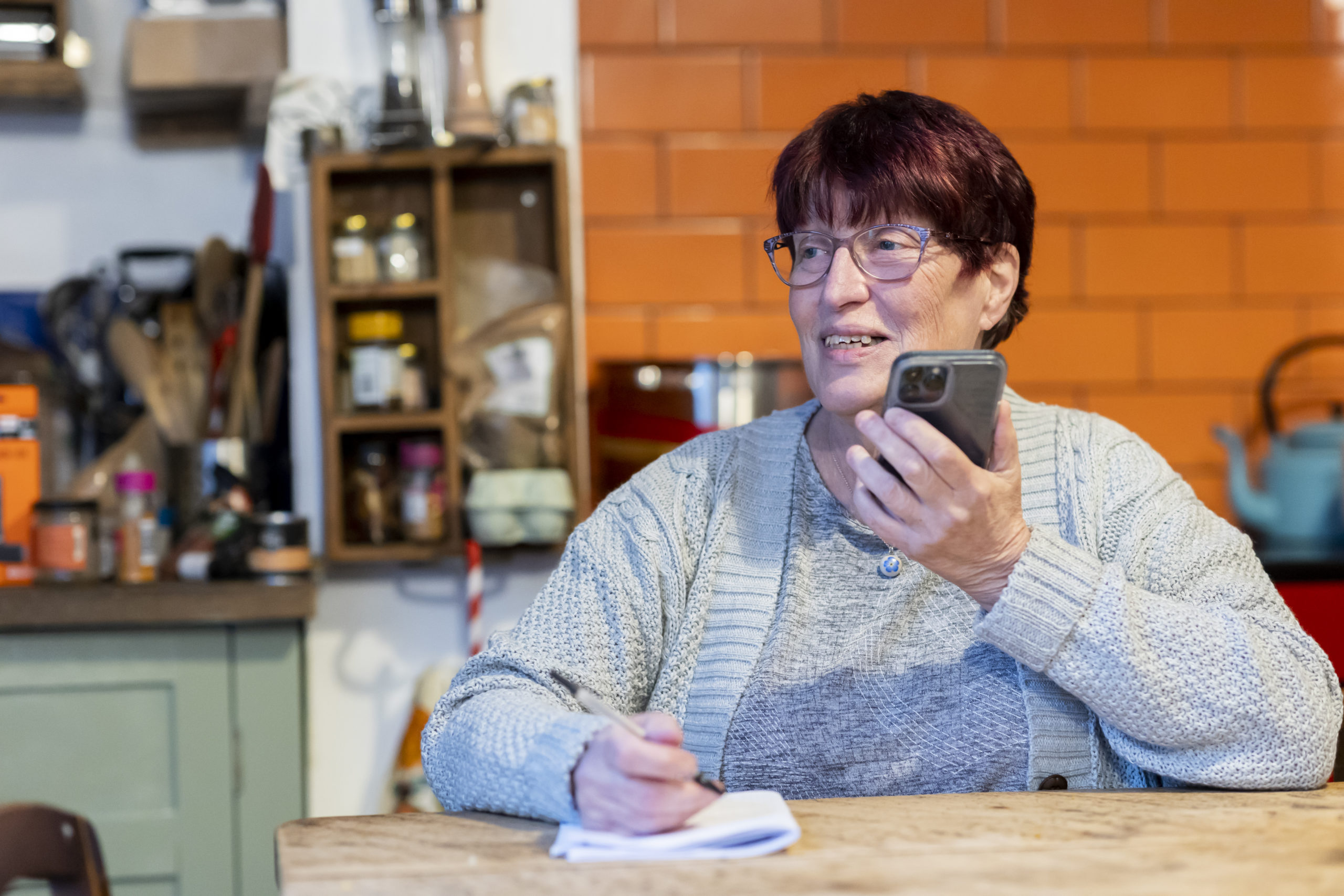 A woman at a table, using her mobile phone to call the Green Energy Helpline