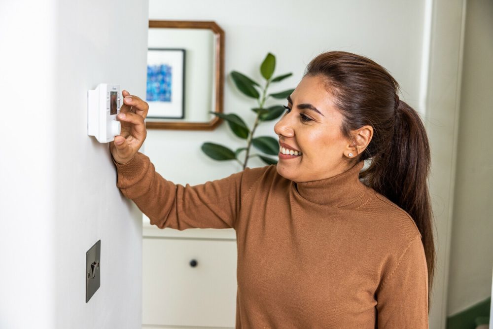 A woman alters the temperature on a thermostat in her home.