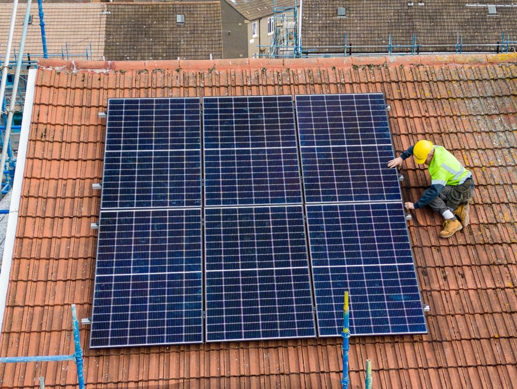 A man wearing a high vis vest on the roof of a house installing solar panels.