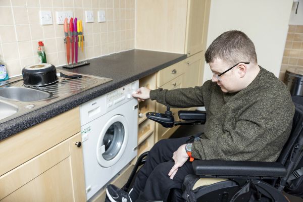 Man adjusting temperature on washing machine, he is a wheelchair user
