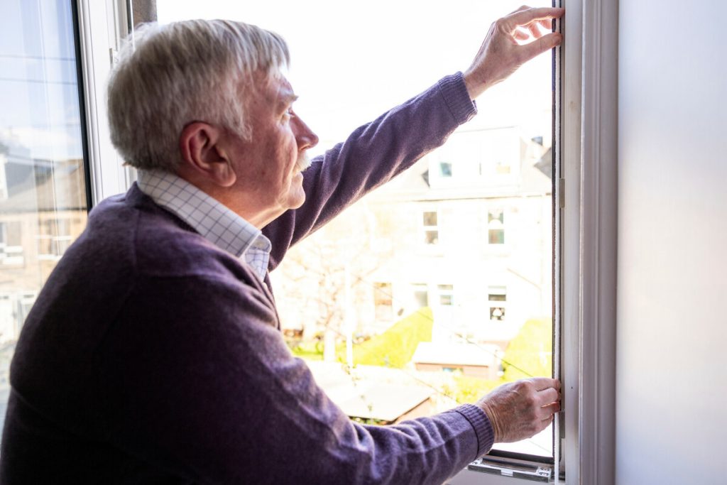 Man attaching draught-proofing strip to right hand side of a window