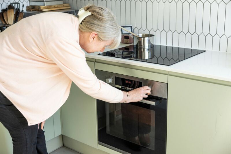 Lady in her kitchen adjusting the temperature on her oven