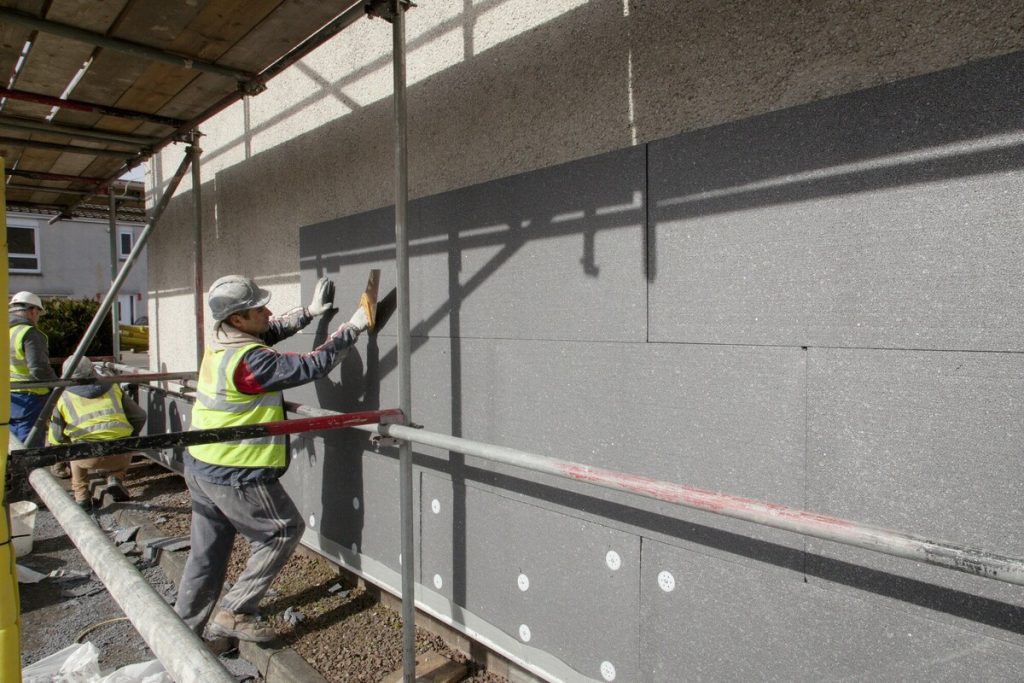 man in high vis attaching external wall insulation to a house