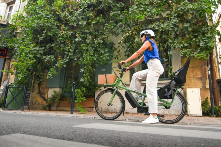 A woman on an e-bike on the road. The e-bike has a child's seat on the back