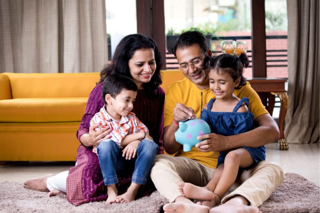 Family of four sitting on the floor of their home with a piggy bank
