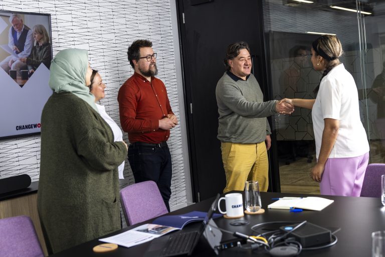 Five colleagues in an office. Two are shaking hands