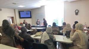A group of women sitting at tables and two women giving a talk
