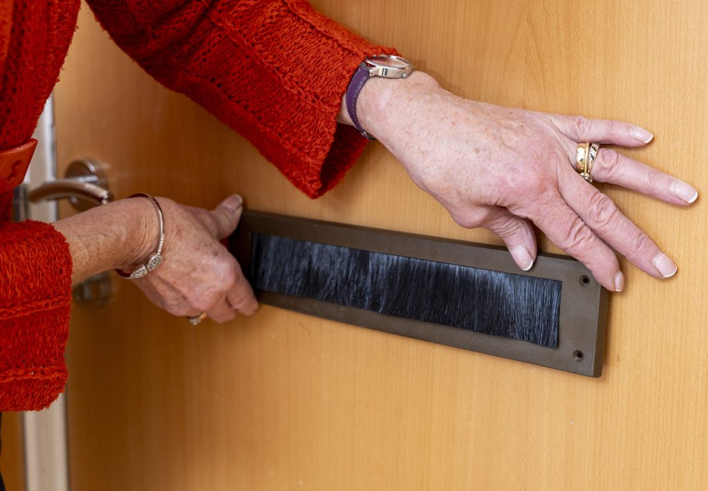 A close up of a person installing a letterbox brush over their letterbox