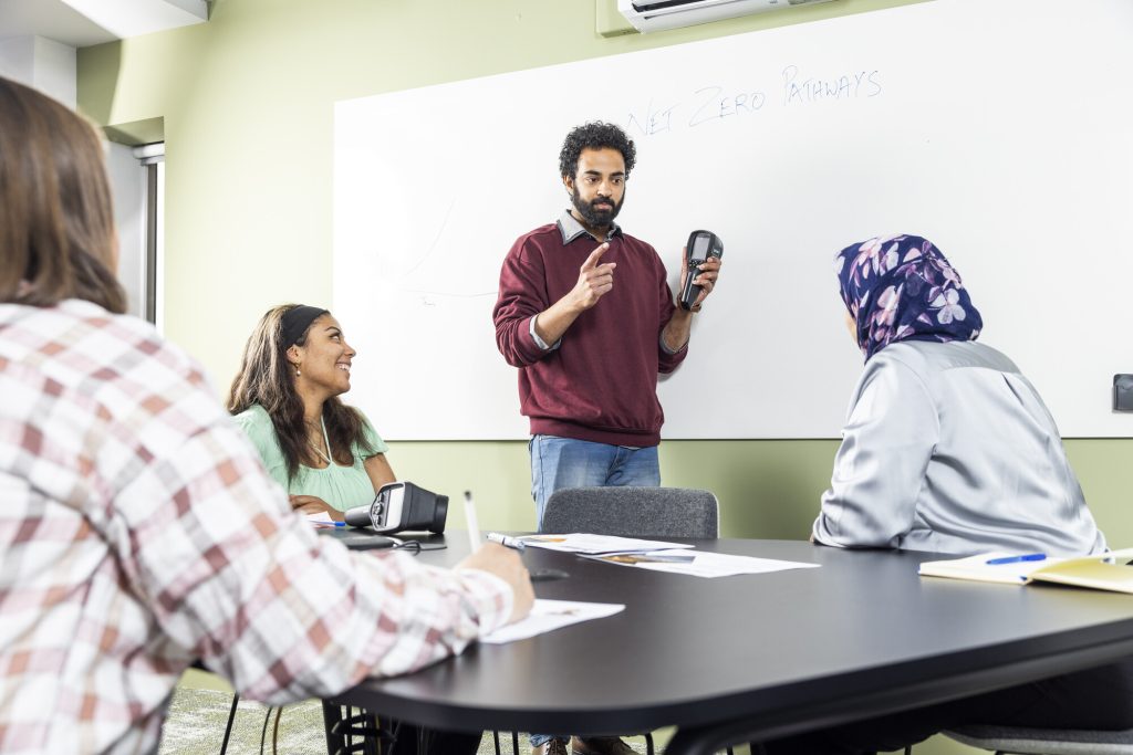 A man in front of a whiteboard and three people sat around a table in an office