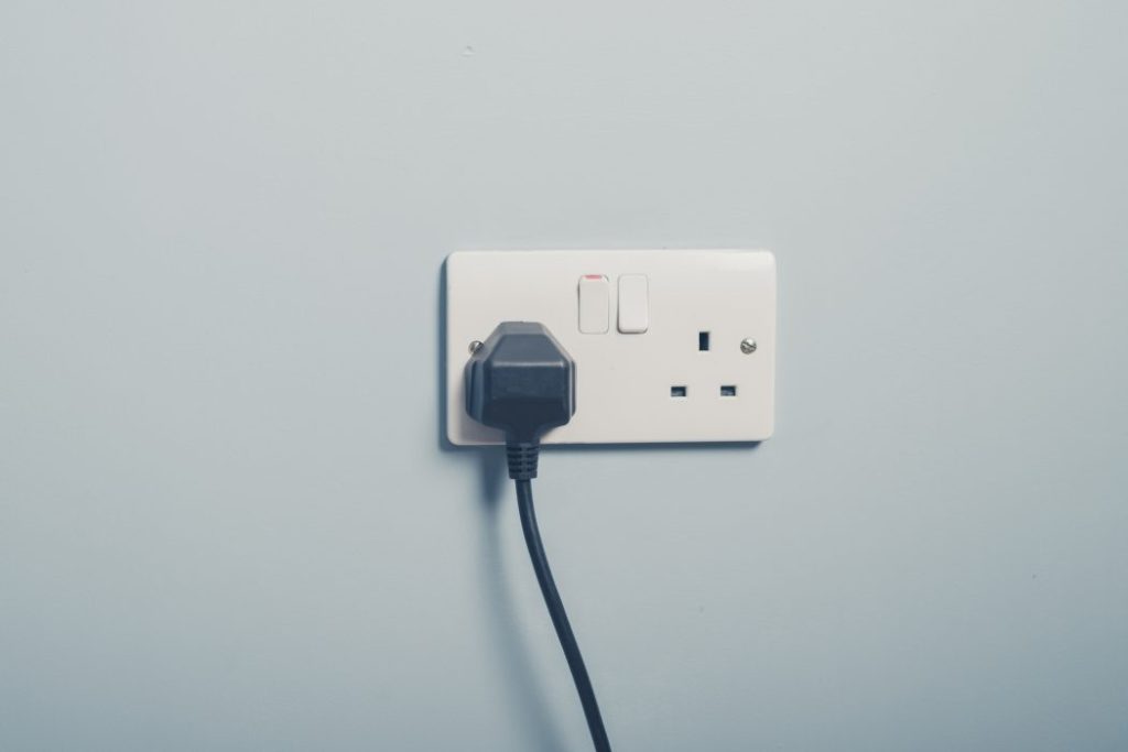 Black plug plugged into a white UK plug socket