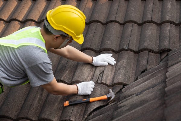 A roofer in a hard hat replacing roof tiles
