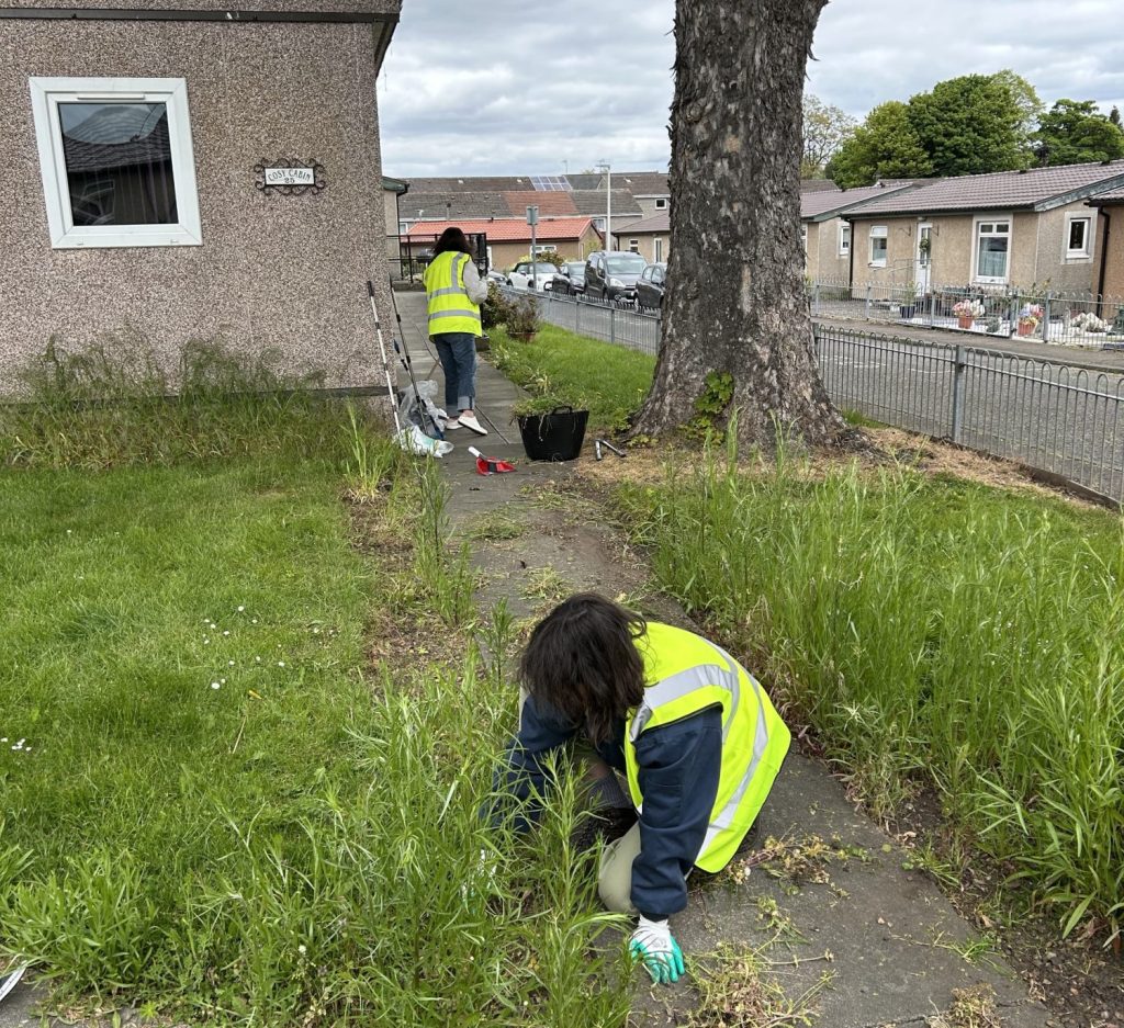 Two volunteers in high viz weeding grass and sweeping a path