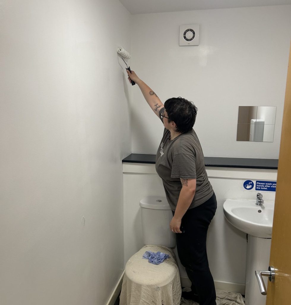 Person using a paint roller to paint a bathroom wall