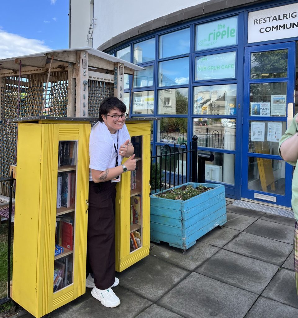Volunteer restocking a little library outside Restalrig community centre
